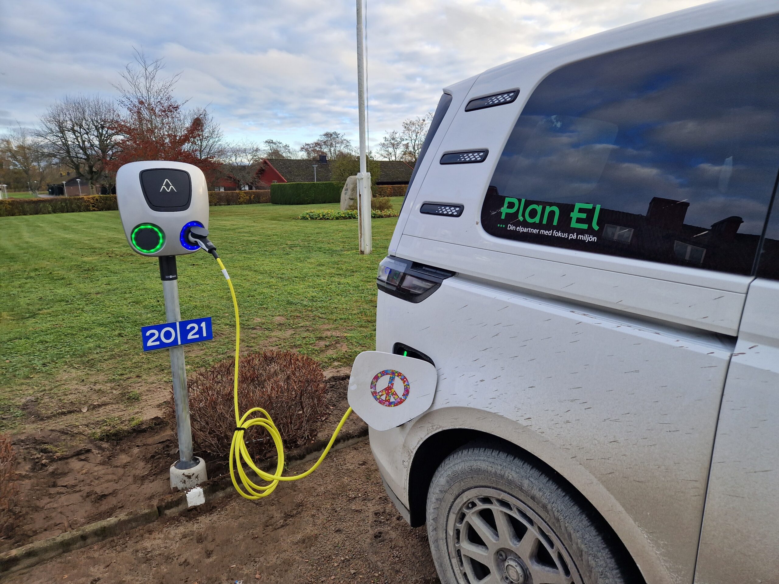Vit bil med med Plan El dekaler som laddar ur en laddstolpe